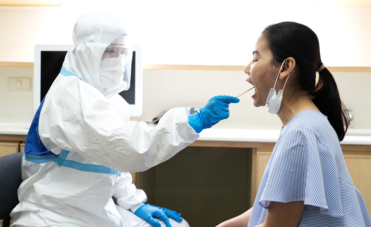 A health worker in protective gear swabs a woman. Experts believe that diagnostic testing remains key to protecting protecting international borders.