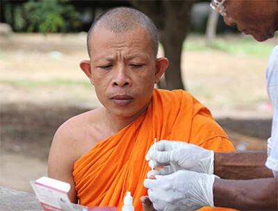 Photo of Venerable Ong Kim Leang, a Buddhist monk, doing a blood test using the Rapid Diagnostic Test from  a volunteer malaria worker at a mobile clinic in Samlot, Cambodia featured in Roche Diagram healthcare magazine publications
